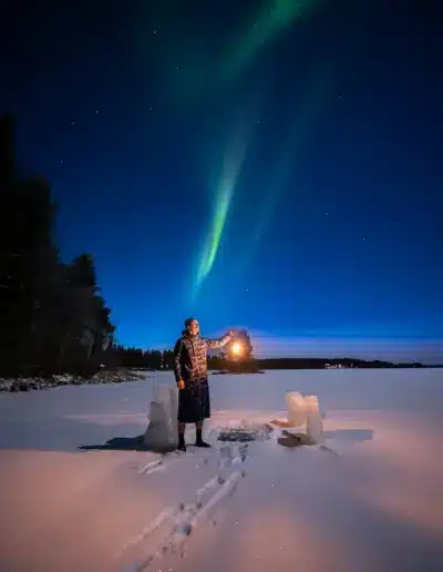 Jarcce seisomassa avannon vieressä revontulien alla jäätyneellä järvellä Suomen Lapissa.